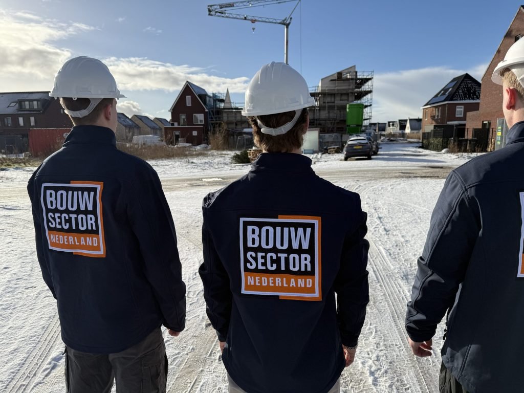 Drie vakmensen van Bouwsector Nederland met witte helm en bedrijfsjas op een besneeuwde bouwplaats